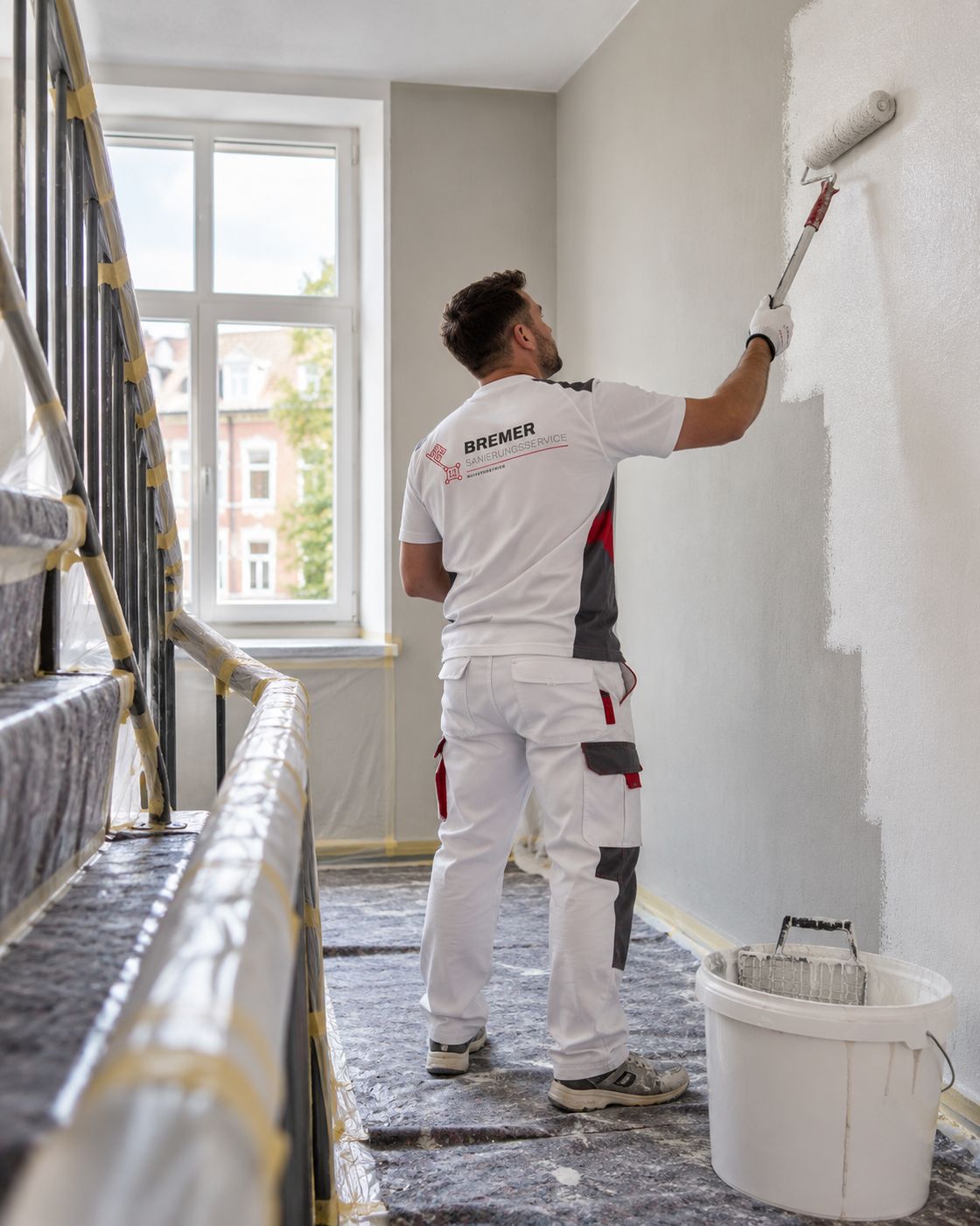 Maler des Bremer Sanierungsservice streicht die Wand in einem Treppenhaus